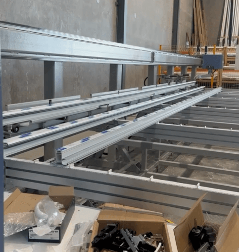 Introducing the SBA-2 CNC Profile Processing Centre 2 A metal framework with multiple rails and support beams is set up indoors, ready for CNC profile processing. Various tools and materials are scattered on a nearby surface, hinting at the intricate craftsmanship underway.