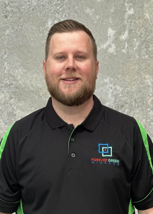 A man in a black and green polo shirt standing in front of a concrete wall.
