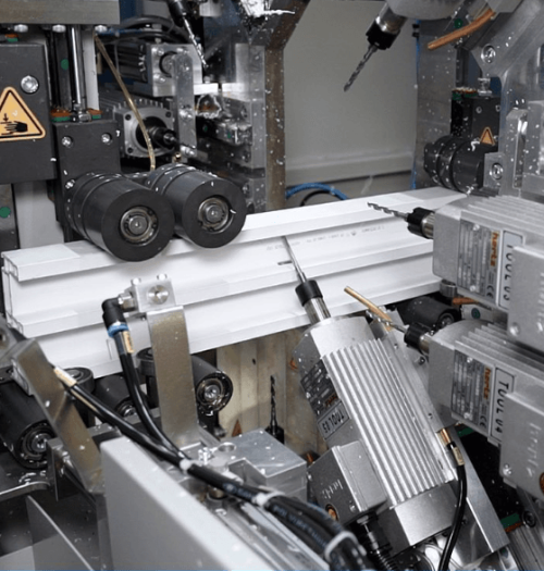 Close-up of an industrial CNC machine expertly performing CNC profile processing, showcasing various components like motors and drill bits as they meticulously shape a white metal workpiece. CNC Profile Processing
