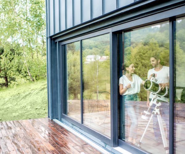 Young couple standing with telescope watching stars near the window in the modern house